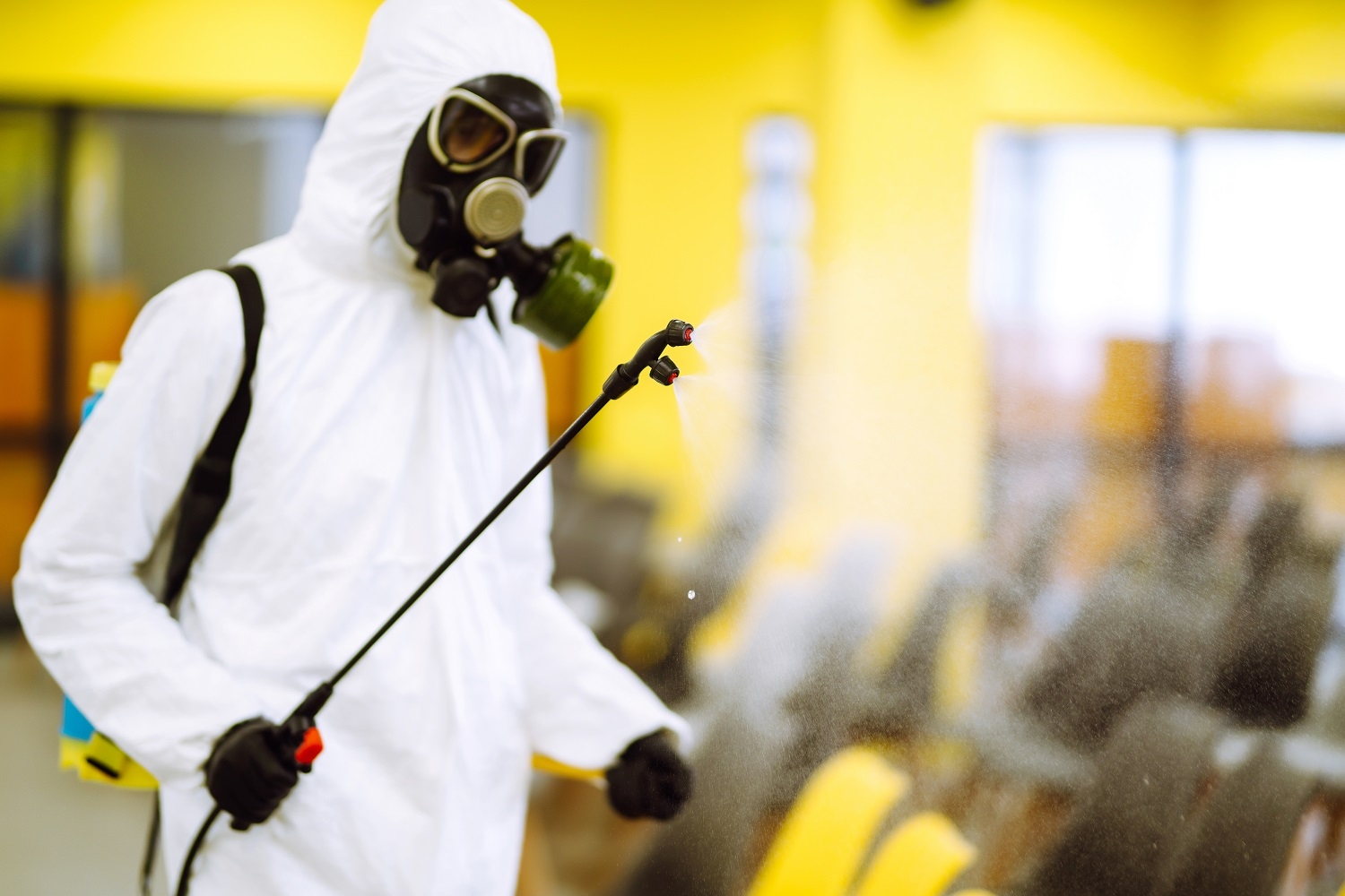 Man wearing protective suit disinfecting assembly hall with spray chemicals to preventing coronavirus.